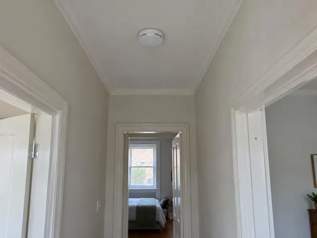 Ceiling smoke alarm in a painted hallway with bedroom doorways and cornices in Kingsford